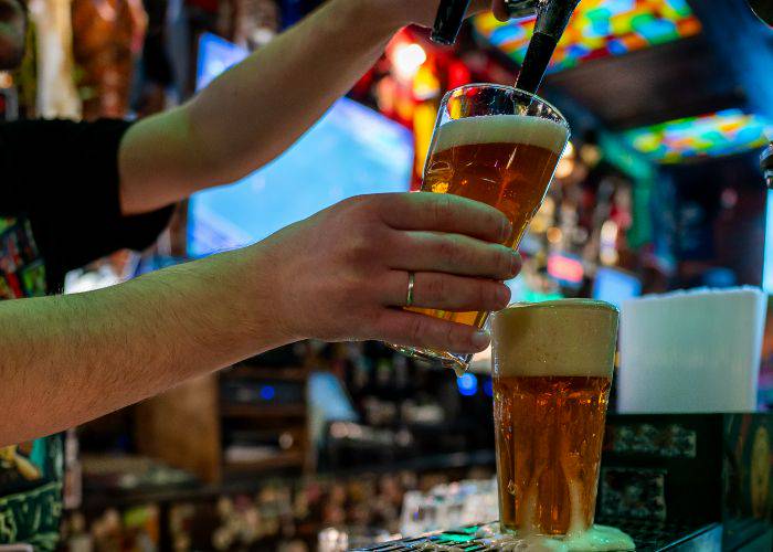 A person pouring a draft pint behind the bar.